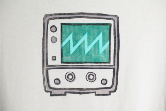 very closeup of the block print of an oscilloscope displaying a sawtooth waveform hand printed centered over the chest area of the t-shirt.