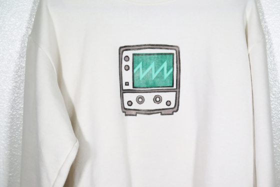 Medium close view of a block print of an oscilloscope displaying a sawtooth waveform is hand printed centered over the front chest area.