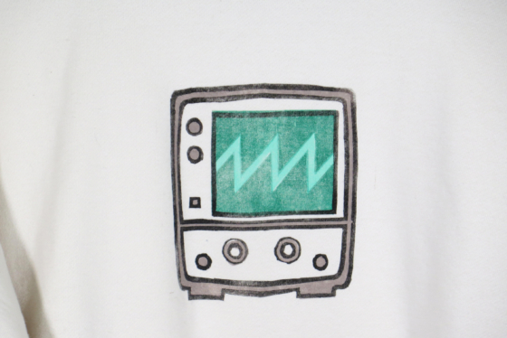Very close view of a block print of an oscilloscope displaying a sawtooth waveform is hand printed centered over the front chest area.