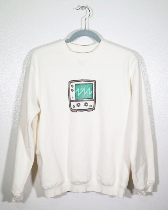 cream sweatshirt on hanger hanging on a nail against a white wall. A block print of an oscilloscope displaying a sawtooth waveform is hand printed centered over the front chest area.