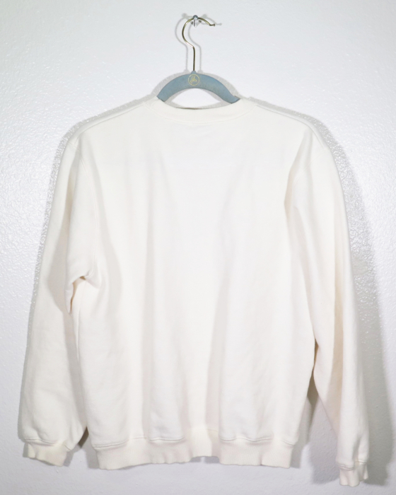 cream sweatshirt on hanger hanging on a nail against a white wall with the back facing the viewer.