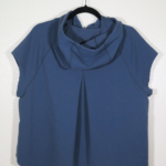 A navy sleeveless hooded shirt on a hanger hangs on a nail against a white wall. Showing the back that has a pleat down the center back.