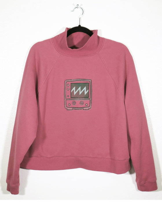 dusty rose sweatshirt on hanger hanging on a nail against a white wall. A block print of an oscilloscope displaying a sawtooth waveform is hand printed centered over the front chest area.