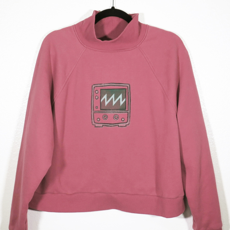 dusty rose sweatshirt on hanger hanging on a nail against a white wall. A block print of an oscilloscope displaying a sawtooth waveform is hand printed centered over the front chest area.