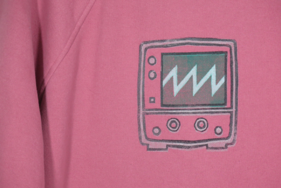Medium close view of a block print of an oscilloscope displaying a sawtooth waveform is hand printed centered over the front chest area.