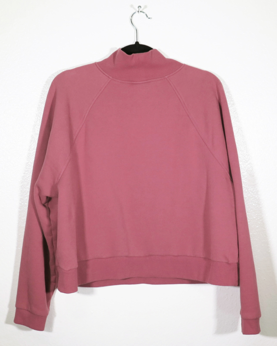 dusty rose sweatshirt on hanger hanging on a nail against a white wall with the back facing the viewer.