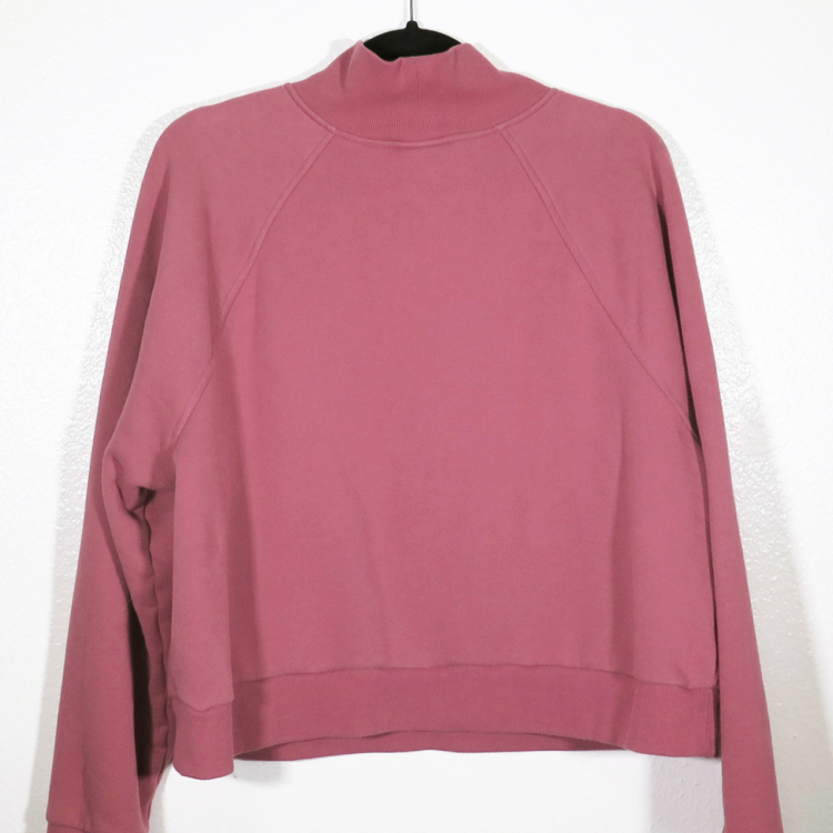 dusty rose sweatshirt on hanger hanging on a nail against a white wall with the back facing the viewer.
