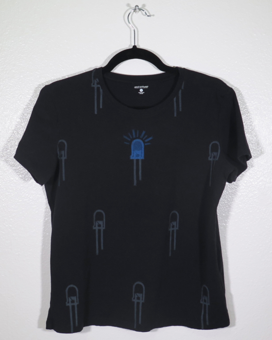 front of black t-shirt on hanger hanging on a nail against a white wall. It is hand printed with an LED design